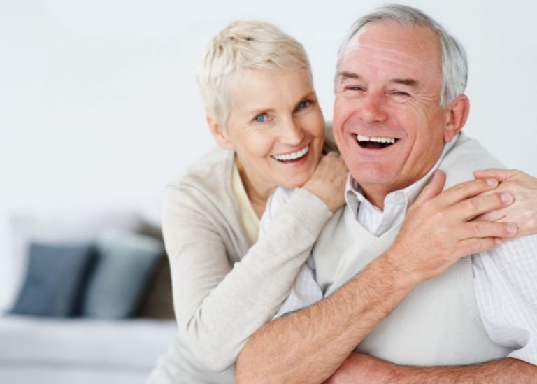 Um casal idoso sorridente abraçando-se, transmitindo felicidade e afeto, em um ambiente doméstico.